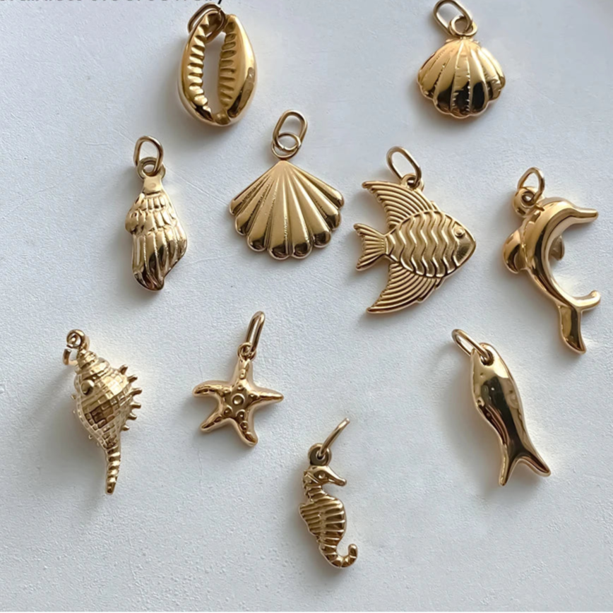 Gold stainless steel jewelry charms on a light gray background with 'Manco' branding.